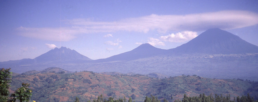 Panoramic view of the Virunga Mountains, showcasing the majestic peaks of Sabinyo, Gahinga, and Muhavura under a clear, azure sky